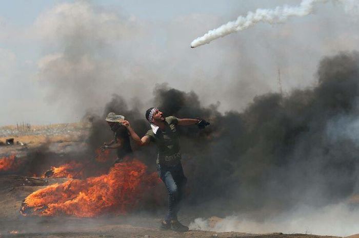 A Palestinian protester uses a tennis racket to deflect a tear gas grenade. - Palestine, Protest, Tennis